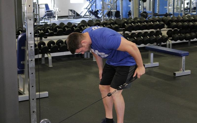 Fit man doing a cable tricep kickback in the gym.