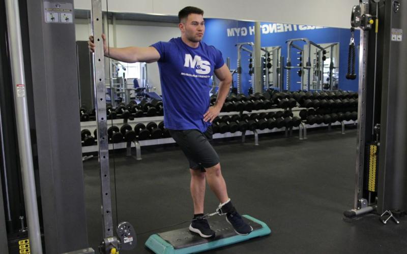 Fit man doing a cable hip adduction in the gym.