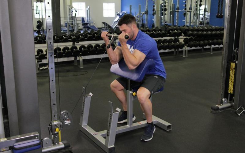 Fit man doing a Cable Preacher Curl in the gym.
