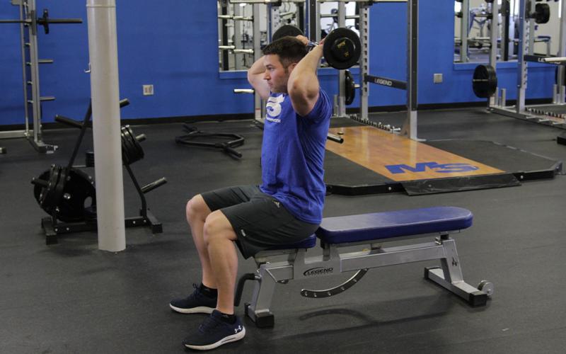 Fit man doing a close grip press behind-the-neck in the gym.