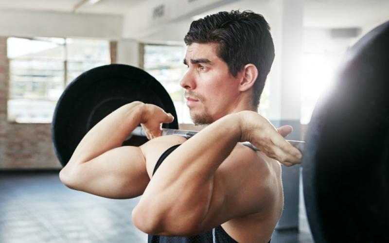 Close up shot of muscular man doing barbell cleans in the gym.