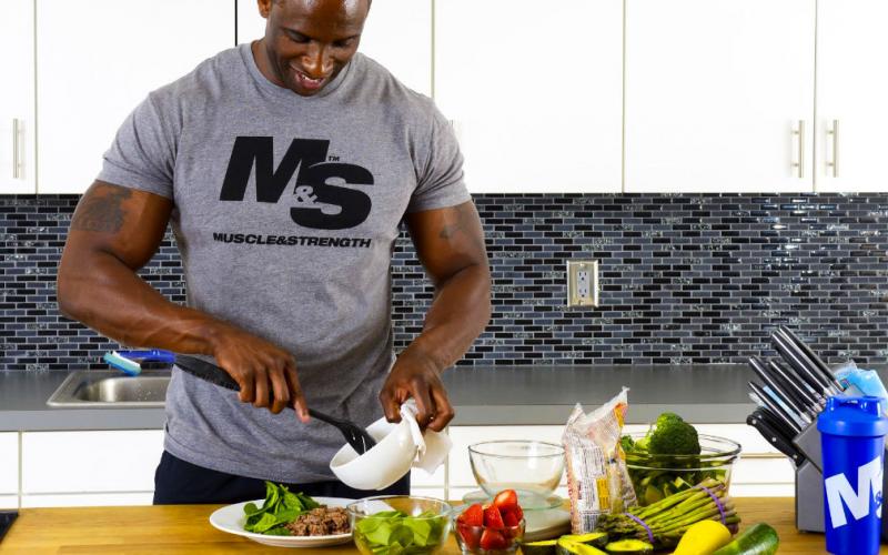 Muscular man in Muscle & Strength t-shirt plating up food.