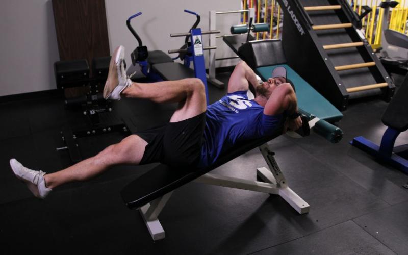Fit man doing a Decline Bench Alternating Knee Raise in the gym.