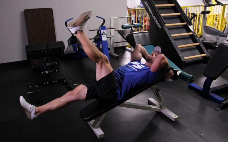 Fit man doing a Decline Bench Alternating Leg Raise in the gym.