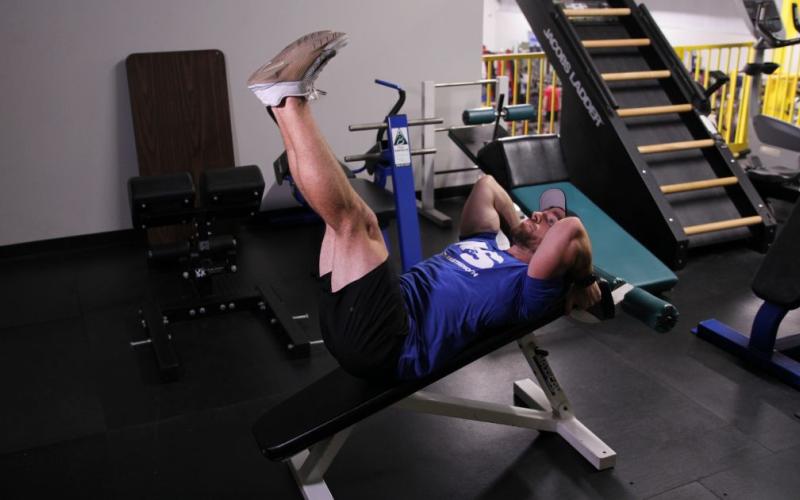 Fit man doing a decline bench leg raise in the gym.