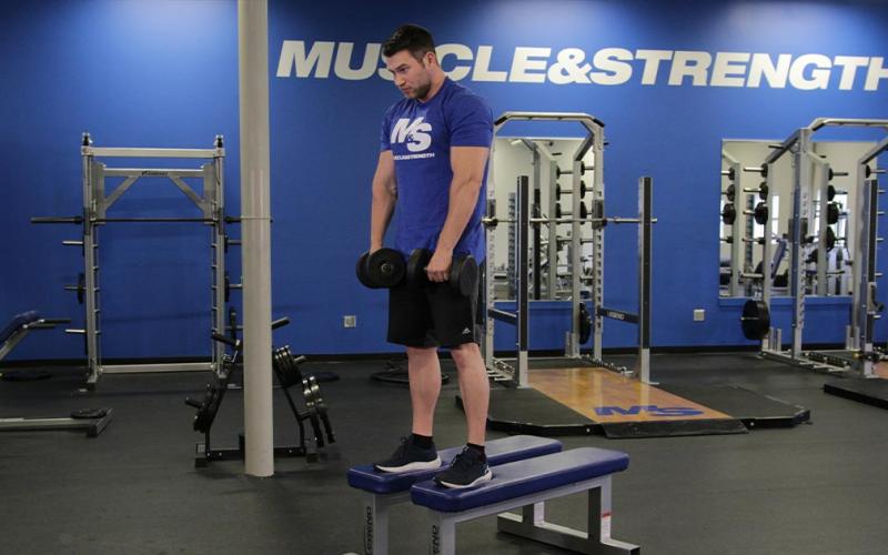 Fit man doing a dumbbell stiff leg deadlift on a bench in the gym.
