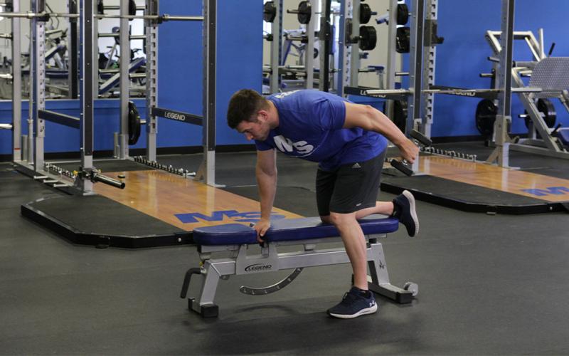 Fit man doing a dumbbell tricep kickback in the gym.