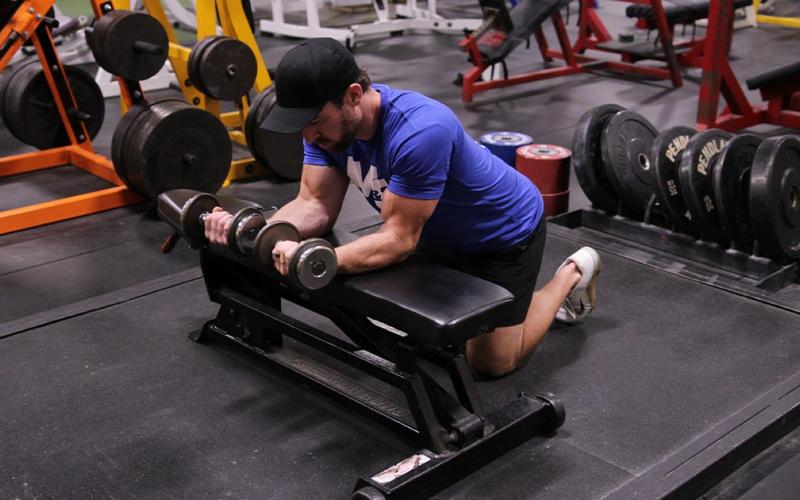 Fit man doing a dumbbell wrist curl over a bench in the gym.