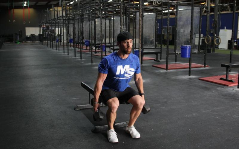 Fit man doing a dumbbell box squat in the gym.
