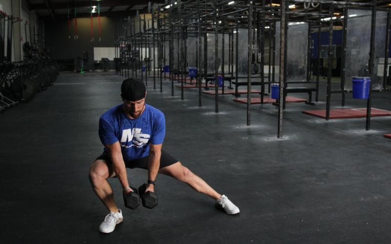 Fit man doing a dumbbell lateral lunge in the gym.