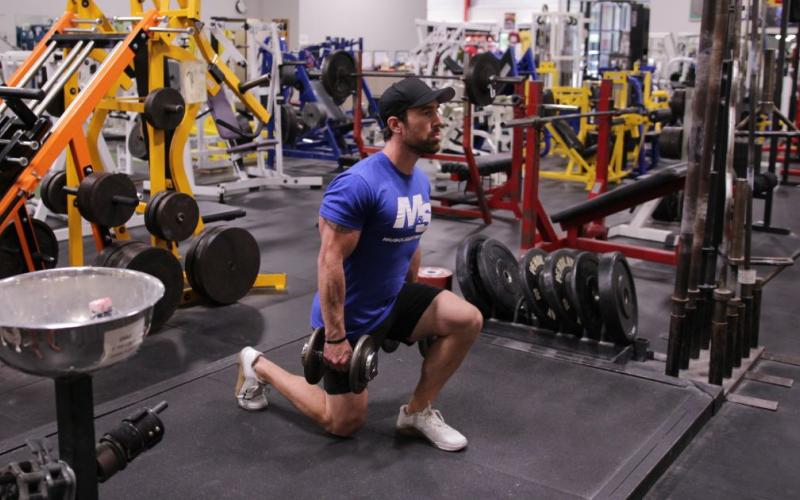 Fit man doing a dumbbell lunge in the gym.