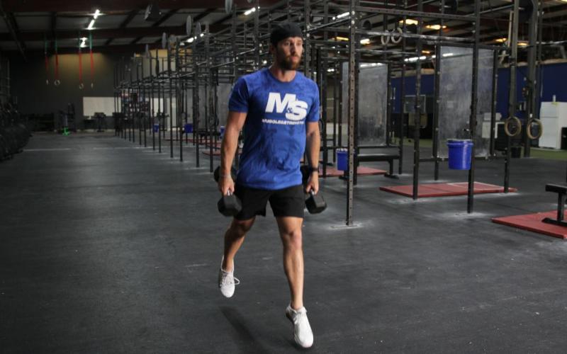 Fit man doing a dumbbell split squat with jump in the gym.