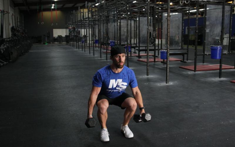 Fit man doing a dumbbell squat in the gym.