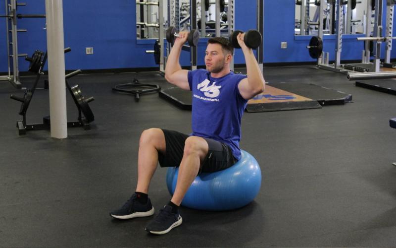 Fit man doing an Exercise Ball Dumbbell Shoulder Press in the gym.