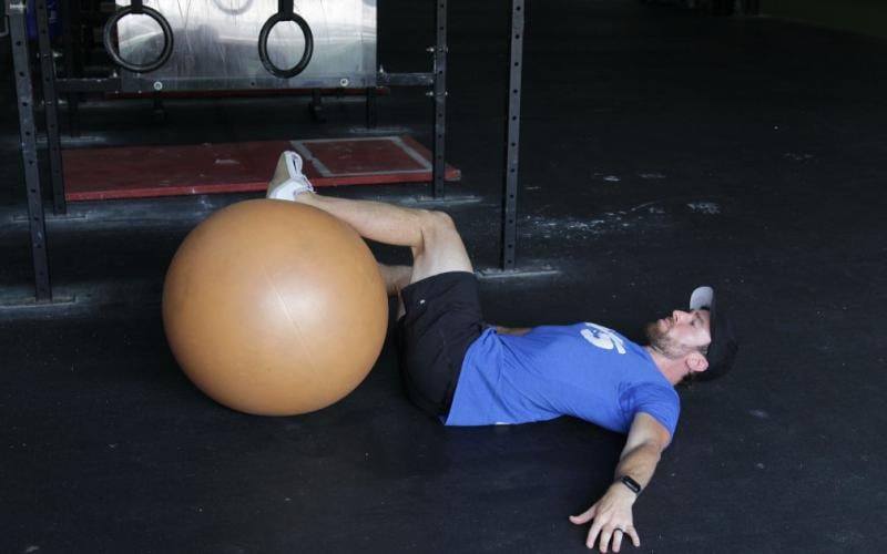 Fit man doing an exercise ball hip roll in the gym.