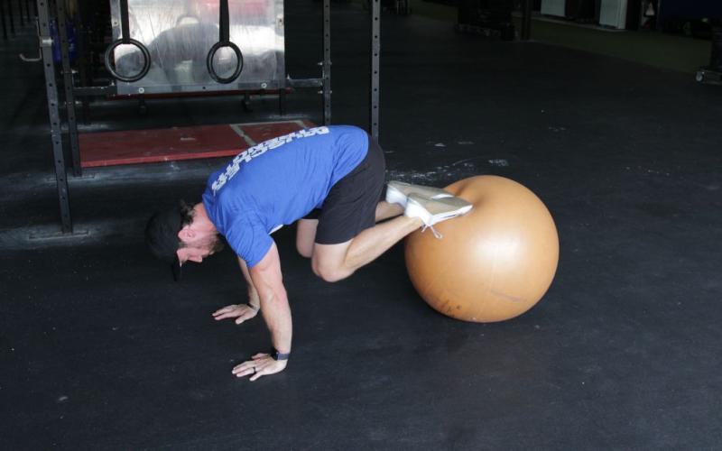 Fit man doing exercise ball knee tucks in the gym.