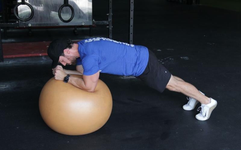Fit man doing Exercise Ball Planks in the gym.