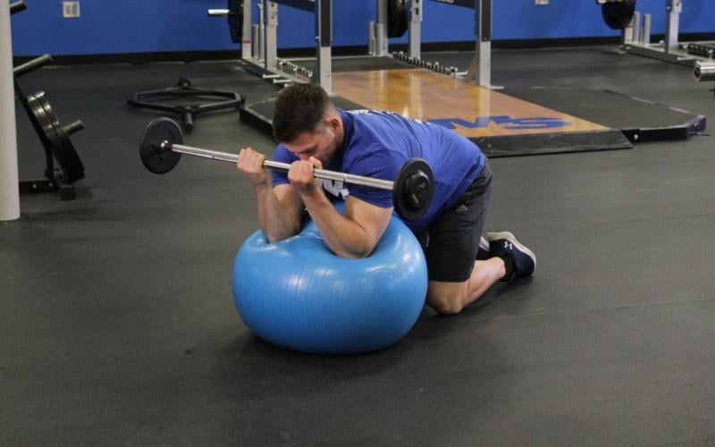 Fit man doing an Exercise Ball Preacher Curl in the gym.