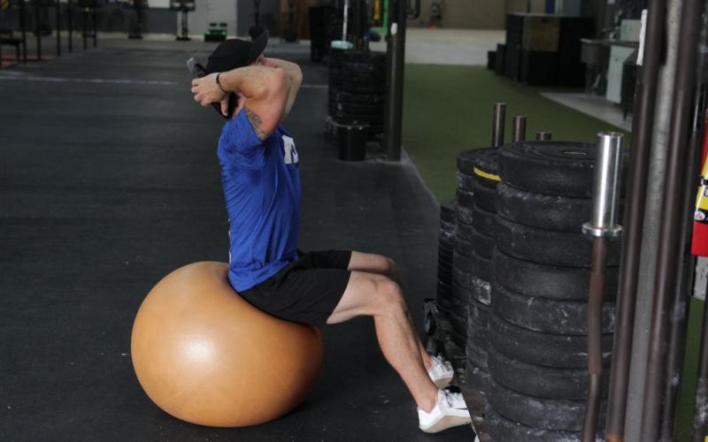 Fit man doing an exercise ball weighted sit up in the gym.