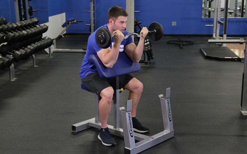 Fit man doing an EZ bar preacher curl at the gym.