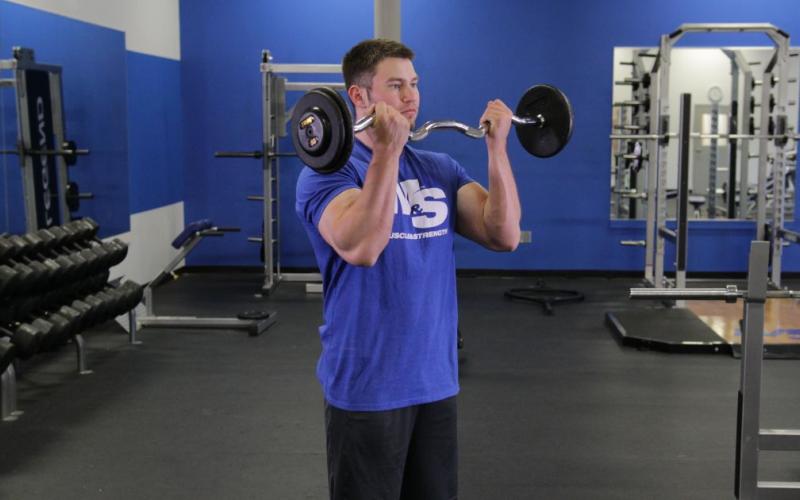 Fit man doing an EZ Bar Curl in the gym