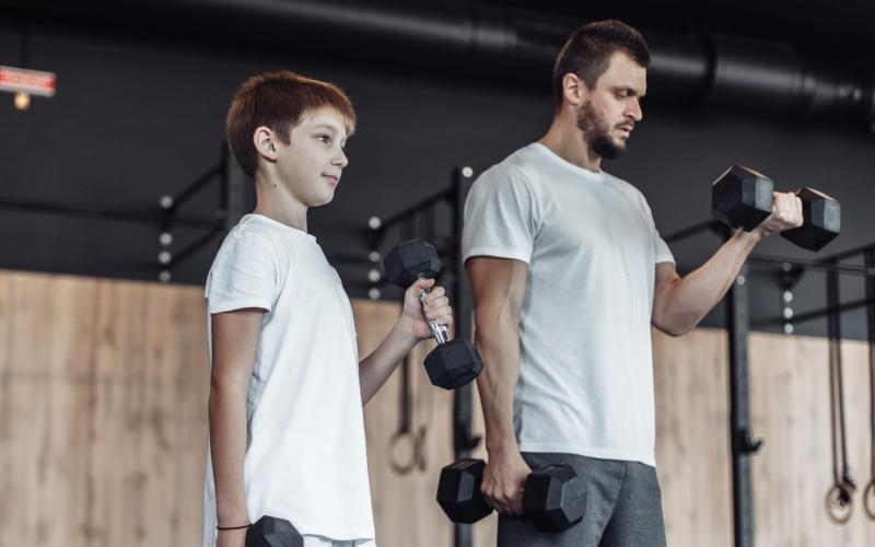 Father and son doing dumbbell bicep curls together in the gym. 