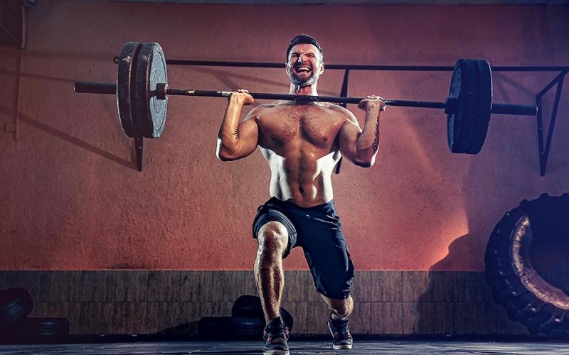 Fit man doing a barbell lunge in the gym.