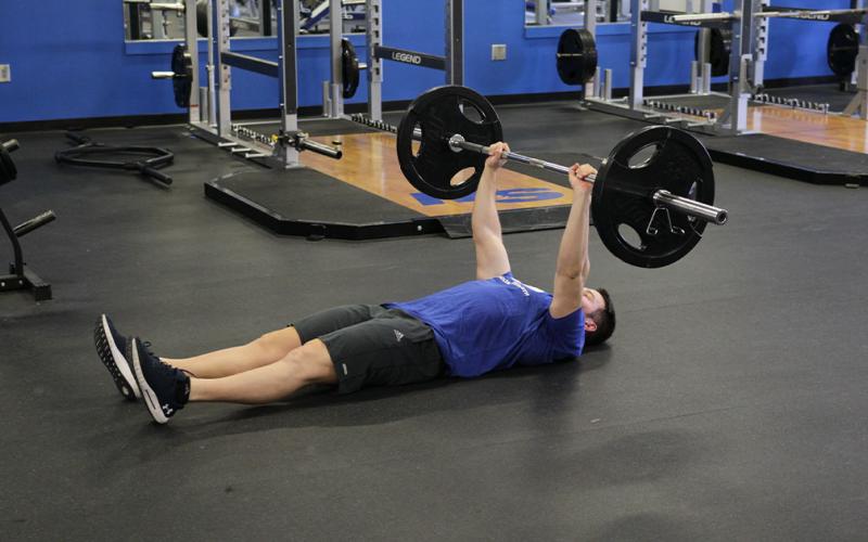 Fit man doing a barbell floor press in the gym.
