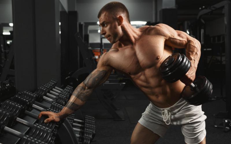 Muscular man doing dumbbell rows in the gym