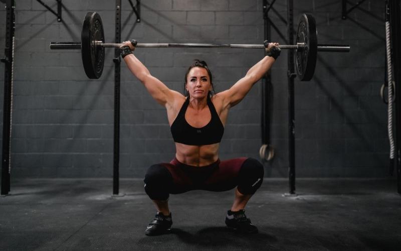 Front shot of strong brunette female doing barbell overhead squats in the gym
