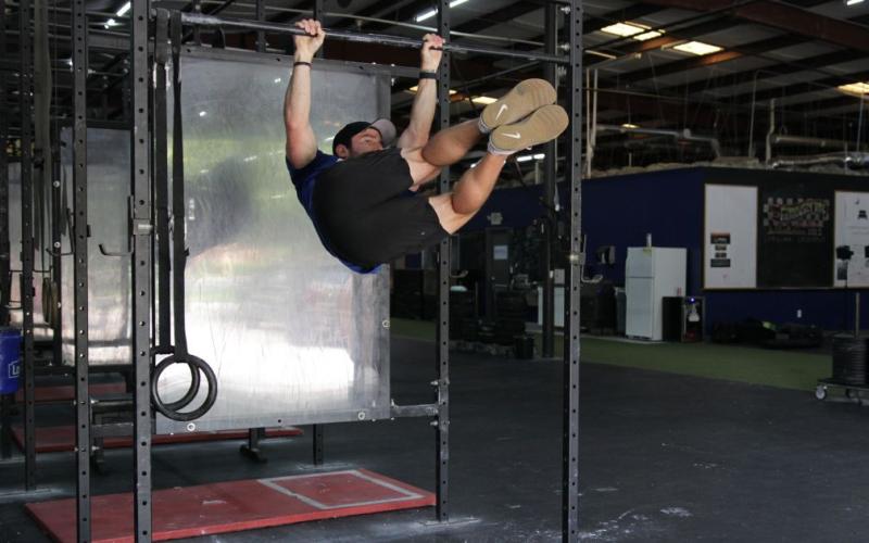 Fit man doing hanging knee raises with a twist in the gym.