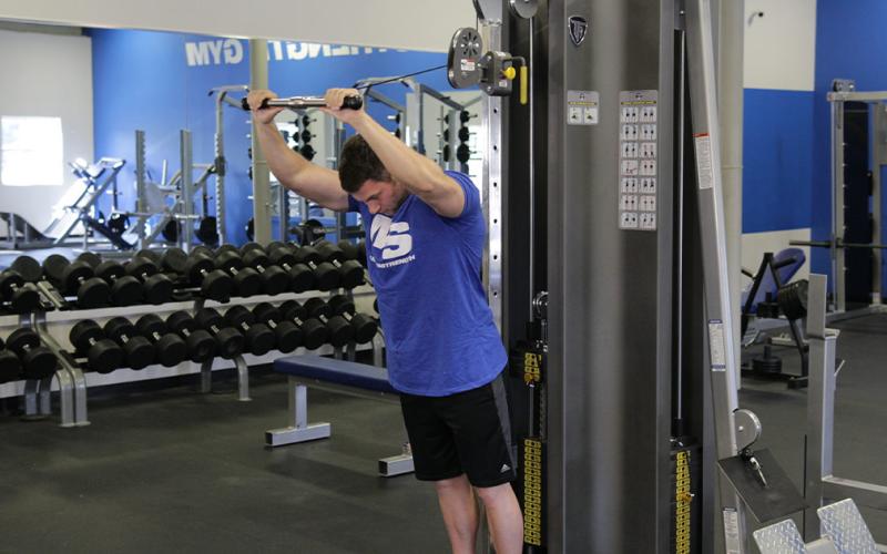 Fit man doing a high pulley overhead tricep extension in the gym,
