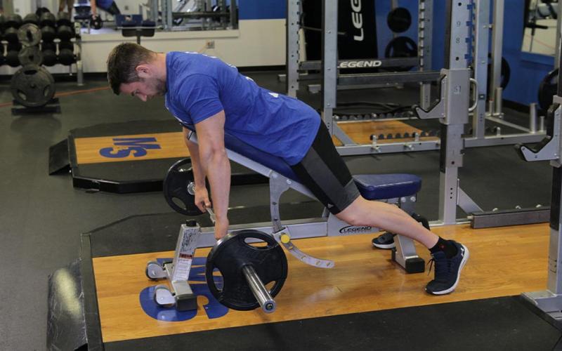 Fit man doing an incline bench barbell row in the gym.