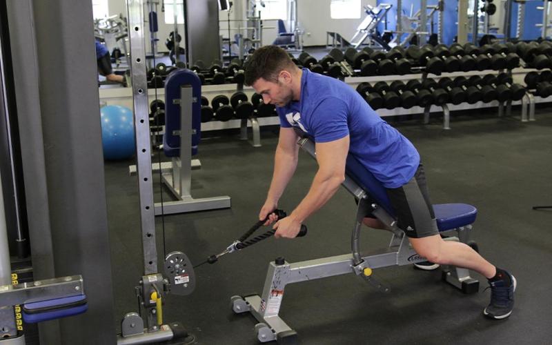 Fit man doing an incline bench cable row with rope extension in the gym.