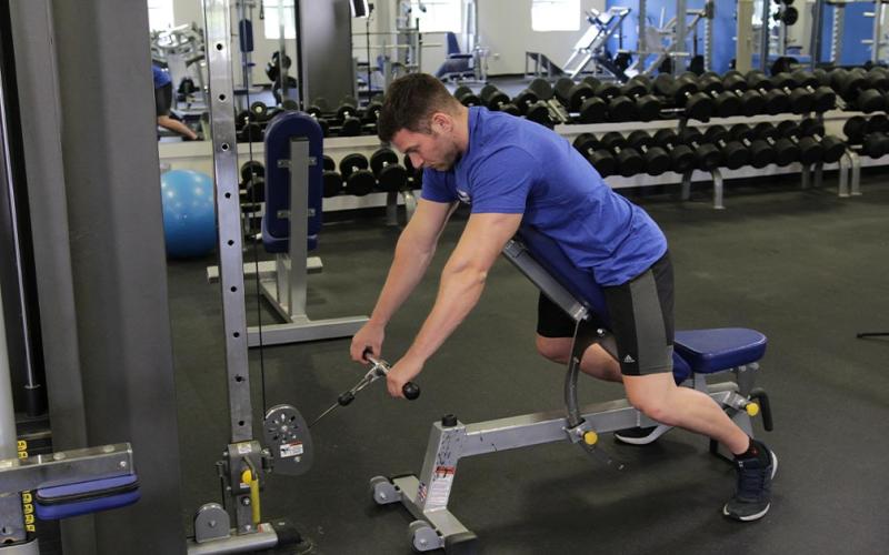 Fit man doing an incline bench cable row in the gym.