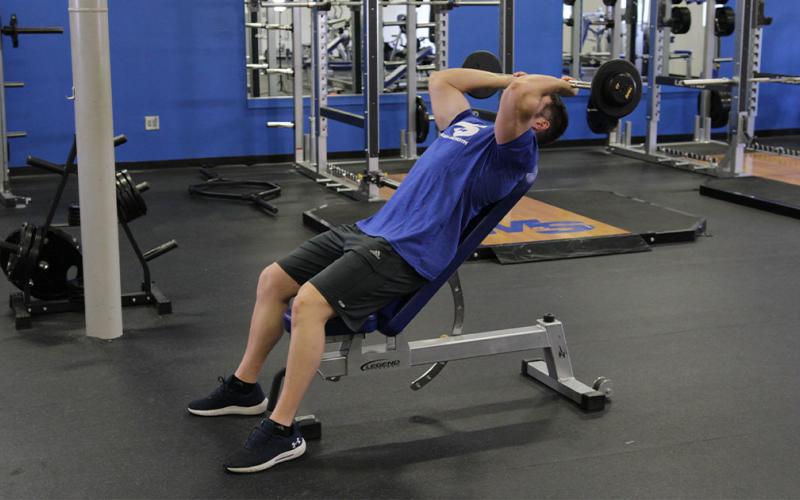 Fit man doing an incline skull crusher in the gym.