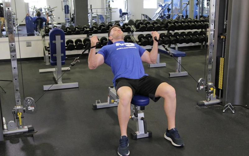 Fit man doing an incline cable bicep curl at the gym.