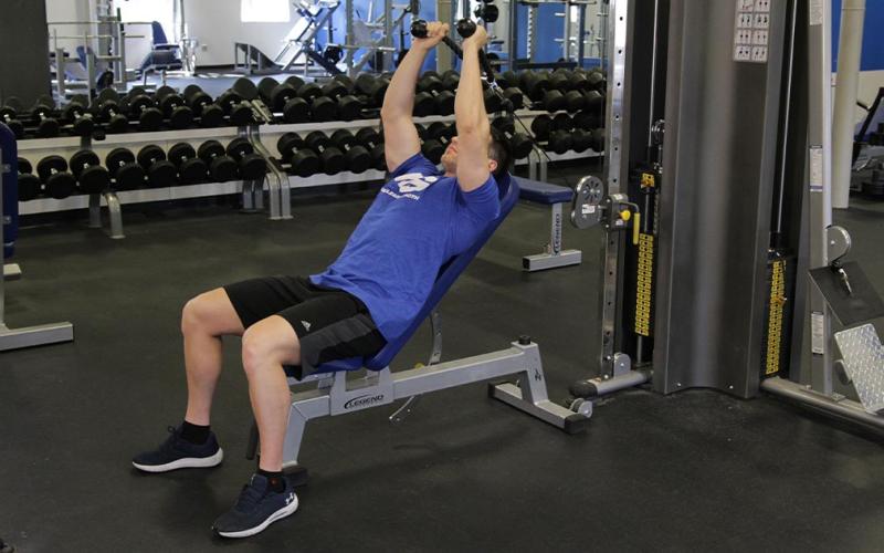 Fit man doing an incline cable tricep extension with rope attachment in the gym.