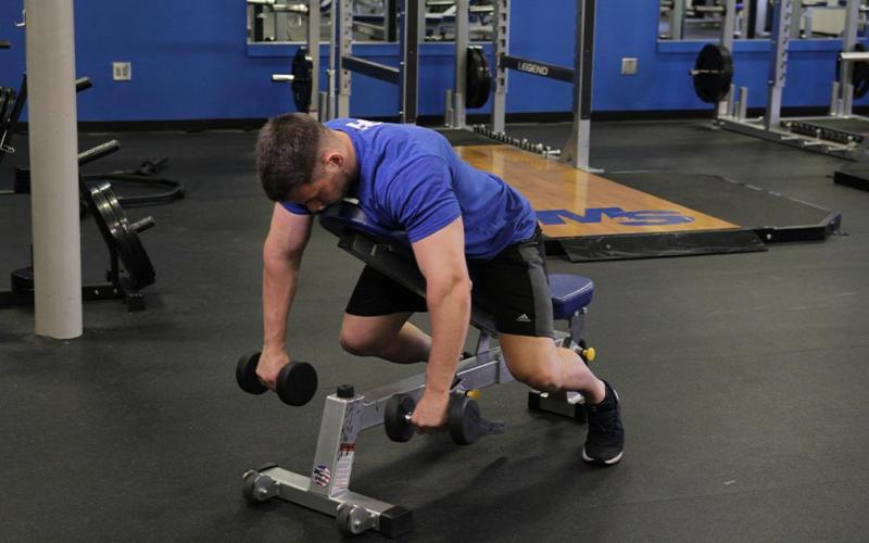 Fit man doing incline reverse dumbbell flys in the gym.