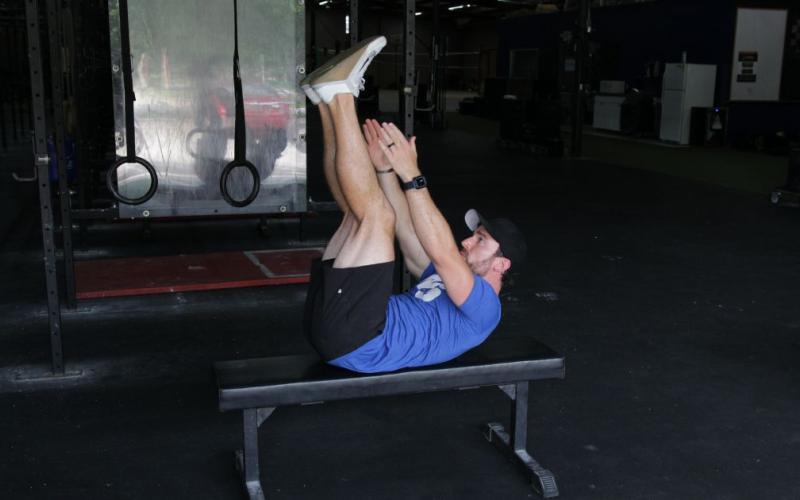 Fit man doing a Jackknife on the bench in the gym.