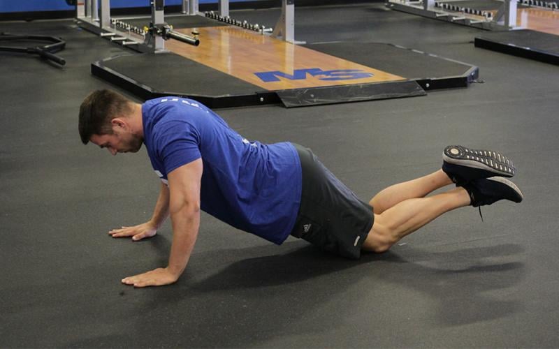 Fit man doing a bodyweight knee push-up in the gym on the floor.