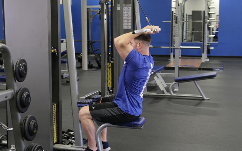 Fit man doing a lateral pulldown with bicep curl in the gym.