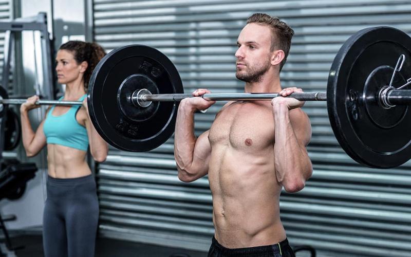 Lean man and woman doing shoulder presses in the gym.