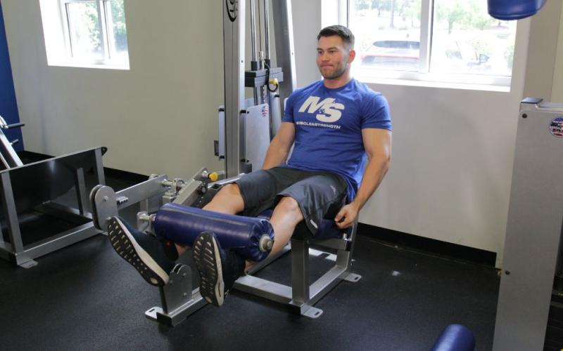 Fit man doing a Leg Extension (Toes Out) in the gym.