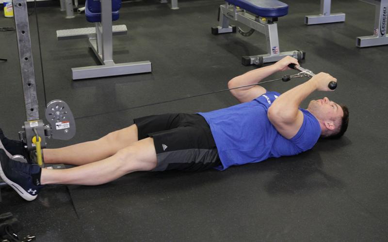 Fit man doing a lying cable curl on the floor in the gym.