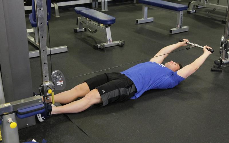 Fit man doing a lying cable front raise in the gym.