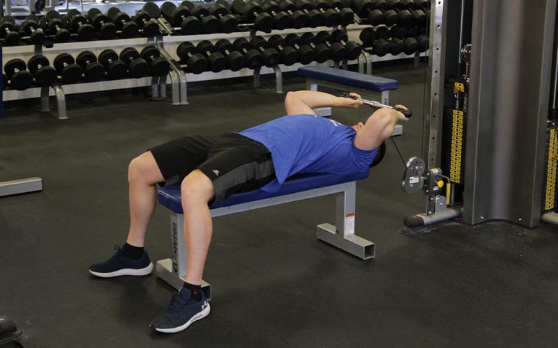 Fit man doing a lying cable tricep extension at the gym.