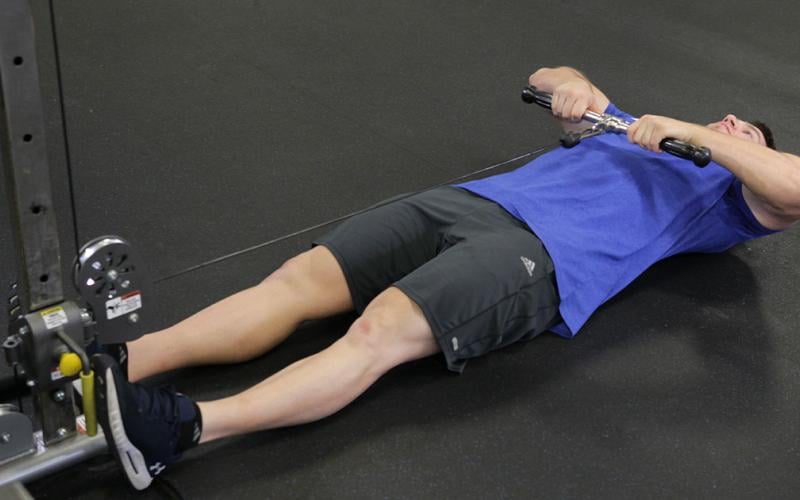 Fit man doing lying cable upright rows in the gym.