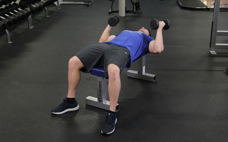 Fit man doing lying dumbbell curls on a bench in the gym.