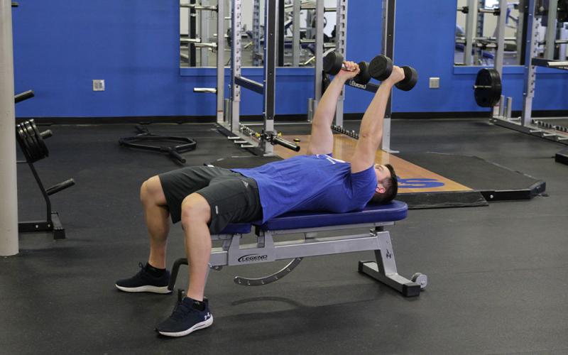 Fit msn doing a Lying Dumbbell Extension in the gym.